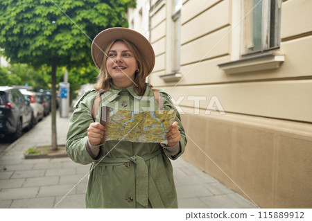 Attractive Caucasian trip woman with big backpack having phone call outdoor, is exploring city with the bulding at the background. . Happy woman holding a paper map and phone on city street.  115889912