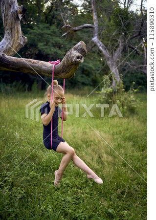 a little 5-year-old gymnast in a black minimalist jumpsuit swings on a gymnastic rope on a tree a little 5-year-old gymnast in a black minimalist jumpsuit swings on a gymnastic rope on a tree 115890310