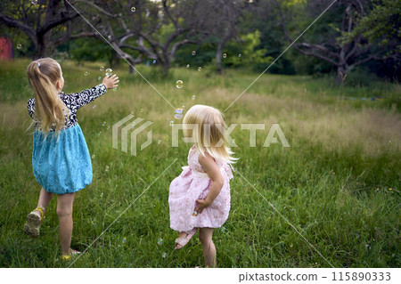 child and toddler, sisters, catching bubbles in the garden 115890333