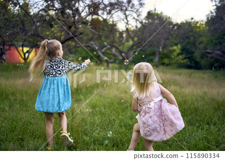 child and toddler, sisters, catching bubbles in the garden child and toddler, sisters, catching bubbles in the garden 115890334