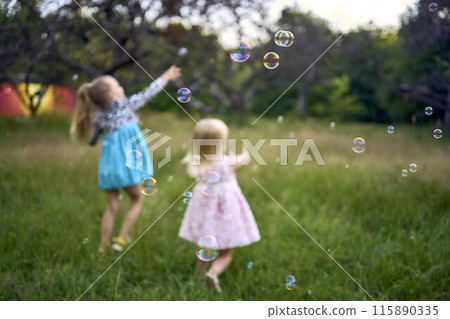 child and toddler, sisters, catching bubbles in the garden 115890335