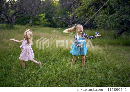 child and toddler, sisters, catching bubbles in the garden 115890341