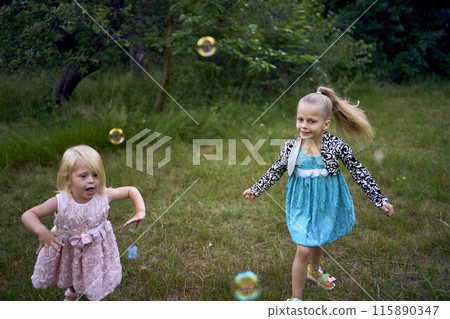 child and toddler, sisters, catching bubbles in the garden 115890347
