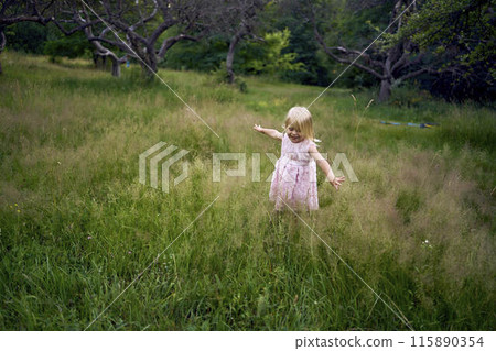a toddler in a pink cloud of a dress runs like an airplane in the garden 115890354