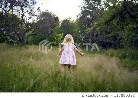 a toddler in a pink cloud of a dress runs like an airplane in the garden 115890358