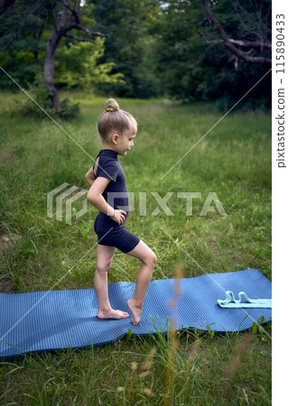 little 5-year-old girl in a black minimalist overall does gymnastics in the garden, outdoors little 5-year-old girl in a black minimalist overall does gymnastics in the garden, outdoors 115890433