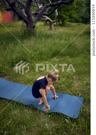 little 5-year-old girl in a black minimalist overall does gymnastics in the garden, outdoors 115890654