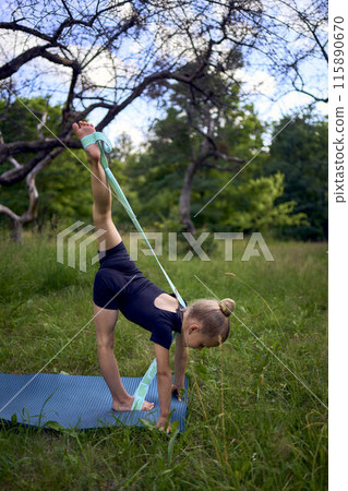 little 5-year-old girl in a black minimalist overall does gymnastics in the garden, outdoors little 5-year-old girl in a black minimalist overall does gymnastics in the garden, outdoors 115890670