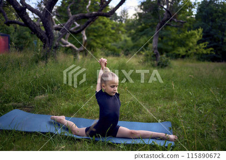 little 5-year-old girl in a black minimalist overall does gymnastics in the garden, outdoors little 5-year-old girl in a black minimalist overall does gymnastics in the garden, outdoors 115890672