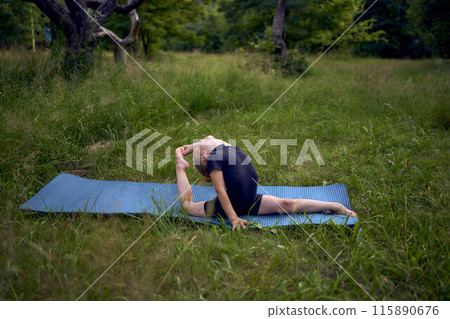 little 5-year-old girl in a black minimalist overall does gymnastics in the garden, outdoors 115890676