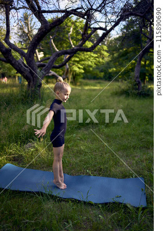 little 5-year-old girl in a black minimalist overall does gymnastics in the garden, outdoors little 5-year-old girl in a black minimalist overall does gymnastics in the garden, outdoors 115890690