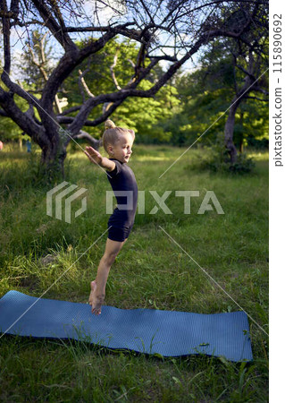 little 5-year-old girl in a black minimalist overall does gymnastics in the garden, outdoors little 5-year-old girl in a black minimalist overall does gymnastics in the garden, outdoors 115890692