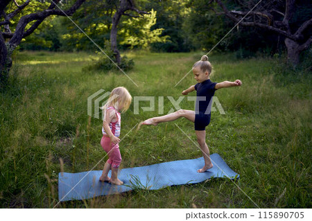 a little 5-year-old gymnast in a black minimalist jumpsuit shows her toddler sister exercises a little 5-year-old gymnast in a black minimalist jumpsuit shows her toddler sister exercises 115890705