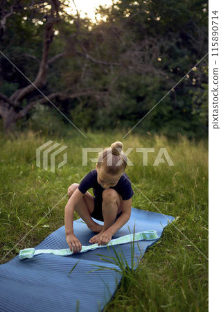 a little 5-year-old girl in a black minimalist jumpsuit does gymnastics in the garden, outdoors 115890714