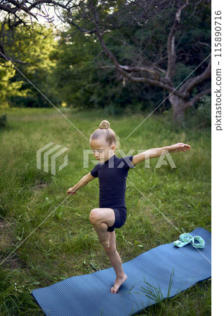 a little 5-year-old girl in a black minimalist jumpsuit does gymnastics in the garden, outdoors a little 5-year-old girl in a black minimalist jumpsuit does gymnastics in the garden, outdoors 115890716