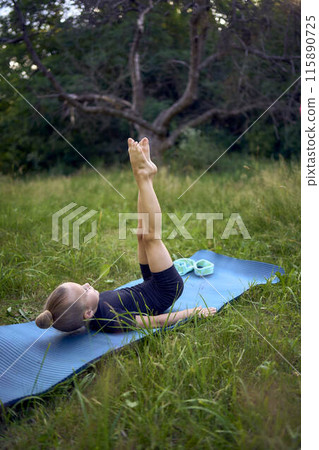 a little 5-year-old girl in a black minimalist jumpsuit does gymnastics in the garden, outdoors 115890725