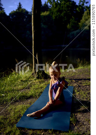 a  llittle 5-year-old girl in a black minimalist jumpsuit does gymnastics by the river, outdoors 115890765