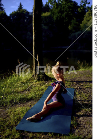 a  llittle 5-year-old girl in a black minimalist jumpsuit does gymnastics by the river, outdoors 115890766