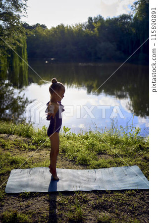 a llittle 5-year-old girl in a black minimalist jumpsuit does gymnastics by the river, outdoors a llittle 5-year-old girl in a black minimalist jumpsuit does gymnastics by the river, outdoors 115890891