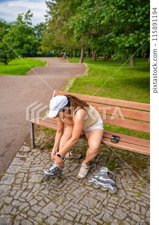 Woman roller skater in the park puts her roller skates on her feet. Outdoor activities. Summer roller skating. Woman roller skater in the park puts her roller skates on her feet. Outdoor activities. Summer roller skating. 115891194