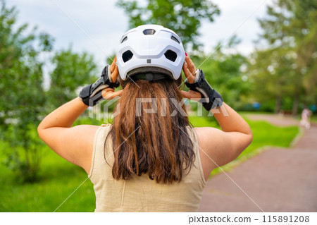 Portrait of roller skater woman putting on helmet in inline skates before rollerblading in park. Outdoor activities. Summer roller skating. 115891208