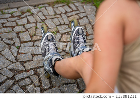View of feet in inline skates of roller skater woman sitting on bench after rollerblading in park. Outdoor activities. Summer roller skating. 115891211