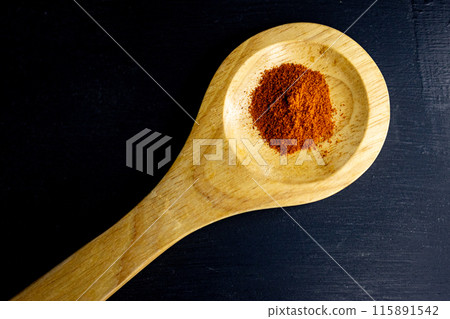 Top view of red paprika on a wooden spoon on black background Top view of red paprika on a wooden spoon on black background 115891542