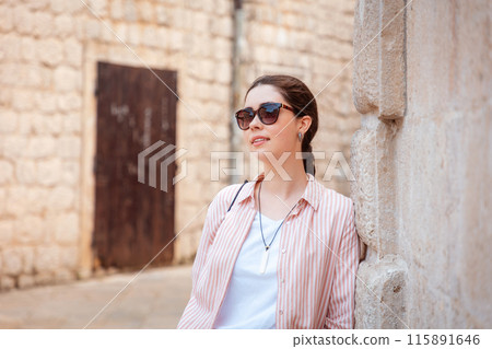 Portrait of young Caucasian woman wearing sunglasses posing in old town leaning on stone wall. Hot summer vacation at Balkans Portrait of young Caucasian woman wearing sunglasses posing in old town leaning on stone wall. Hot summer vacation at Balkans 115891646