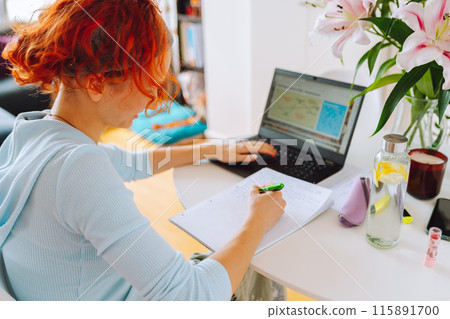 portrait red-haired teenage girl sitting at table in room using computer 115891700