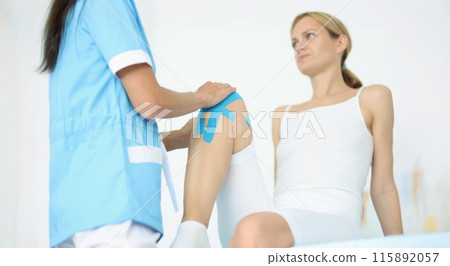 Doctor fixes kinesio tape on female leg Doctor fixes kinesio tape on female leg 115892057