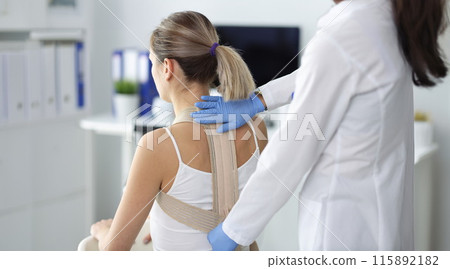 Doctor fixes posture corrector to patient closeup Doctor fixes posture corrector to patient closeup 115892182
