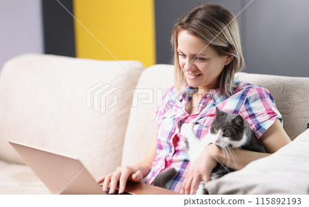 Woman with cat is sitting on couch and working on laptop 115892193