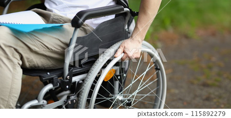 Man in wheelchair holds wheel with his hand 115892279