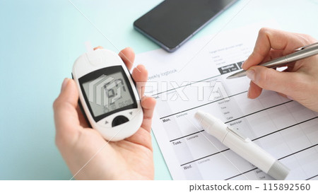 Patient holding glucometer and recording data in diary closeup 115892560