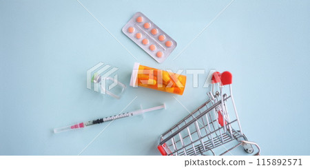 Many medicines and syringe lying near toy metal basket closeup 115892571
