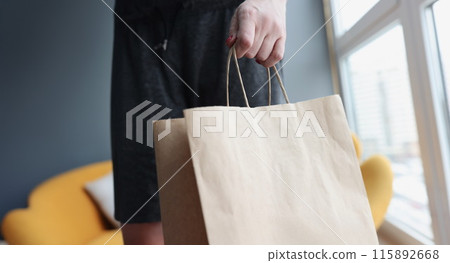 Woman hand holding paper bag at home closeup Woman hand holding paper bag at home closeup 115892668