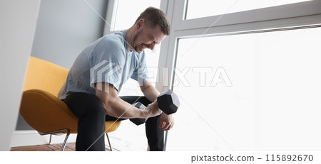 Young man sitting on chair and lifting heavy dumbbell Young man sitting on chair and lifting heavy dumbbell 115892670