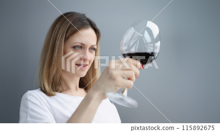 Young woman looking into glass with red wine Young woman looking into glass with red wine 115892675