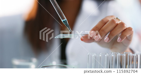 Scientist dripping blue liquid from pipette onto glass slide closeup Scientist dripping blue liquid from pipette onto glass slide closeup 115892704