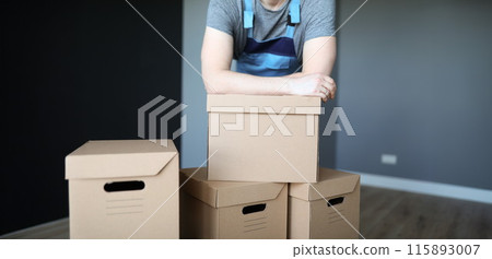 Man in overalls putting his hands on cardboard boxes closeup Man in overalls putting his hands on cardboard boxes closeup 115893007