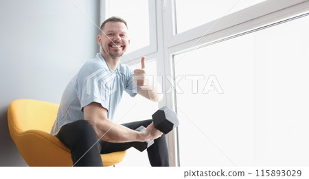 Portrait of smiling man holding dumbbells and showing thumbs up gesture 115893029