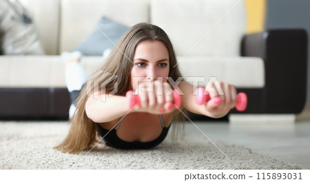 Young woman in sportswear lying on floor and holding dumbbells in her hands 115893031