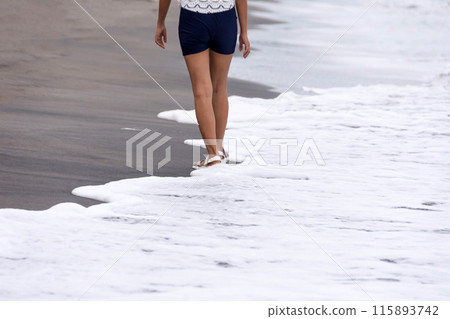 Legs of a girl in sandals walking alone along a sandy beach along the sea Legs of a girl in sandals walking alone along a sandy beach along the sea 115893742