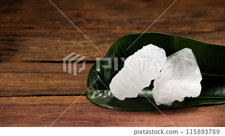 A basket filled with white alum crystals sits on a vibrant green shrub background. 115893789