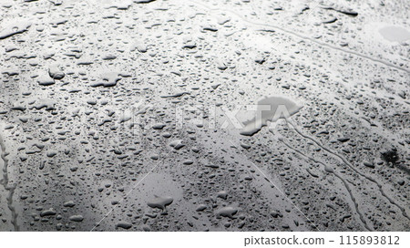 This image captures raindrops on a dark surface, highlighting their glistening clarity and natural beauty. 115893812