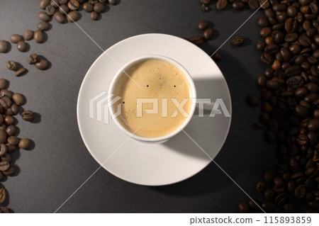 white cup with espresso coffee on a saucer with coffee beans on a dark background 115893859
