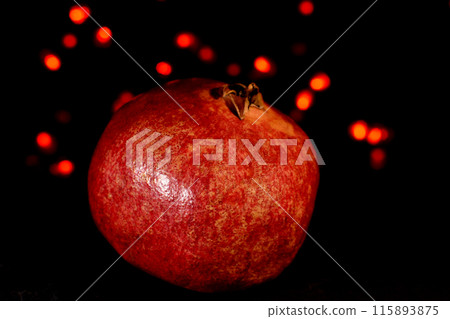 pomegranate fruit close up on a black background with glowing lights in the background 115893875