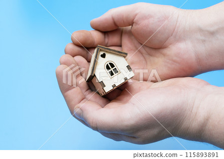 small wooden house in human palms on a blue background small wooden house in human palms on a blue background 115893891