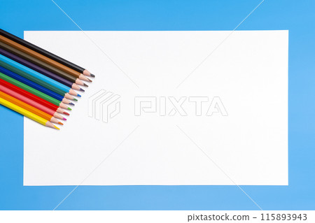 colored pencils and a white empty sheet of paper on a blue background colored pencils and a white empty sheet of paper on a blue background 115893943