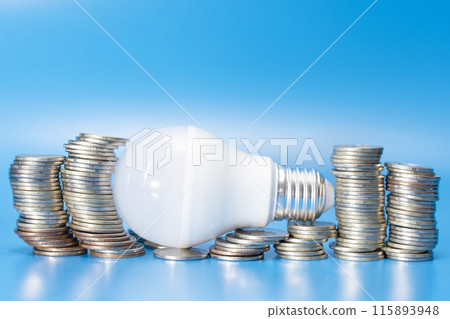 led lamp on stacks of coins on a blue background. energy saving. economy. led lamp on stacks of coins on a blue background. energy saving. economy. 115893948